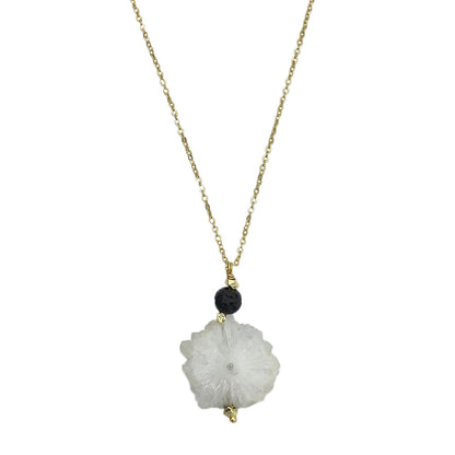 Necklace with a white floral pendant and black bead on a gold chain against a white background