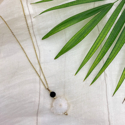 Necklace with a quartz crystal pendant and black bead on a white fabric background with green leaves.